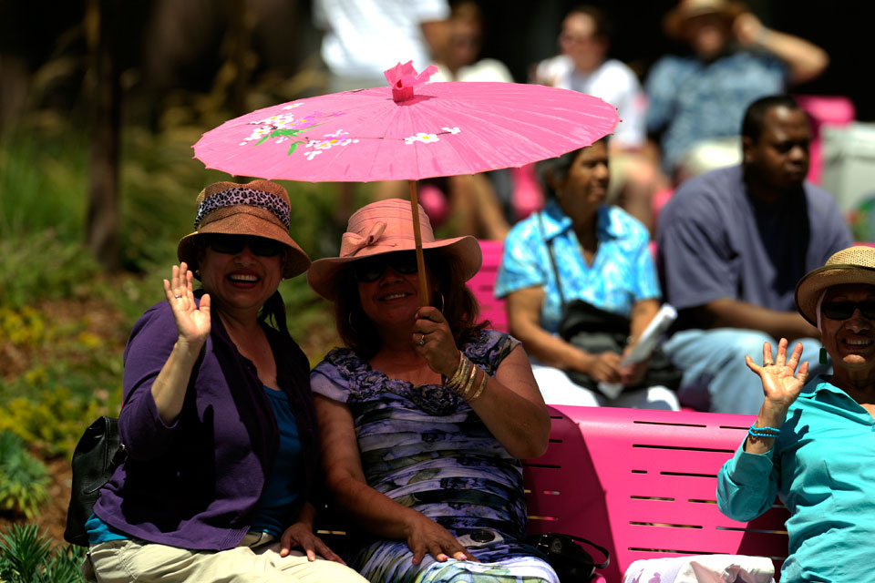 Two smiling women under an umbrella, waving at the camera